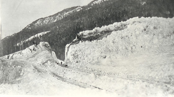 Photographie en noir et blanc d'hommes qui déblaient d'énormes quantités de débris d'avalanche recouvrant un chemin de fer.