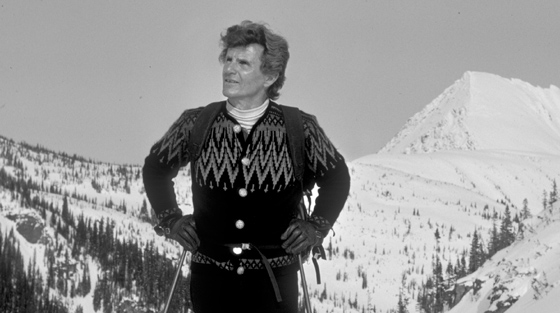 Close-up black and white photograph of man with ski poles standing at summit of mountain.