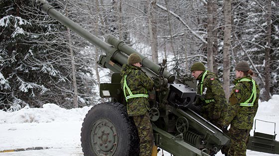 Colour photograph of 3 Canadian army professionals operating howitzer in snow covered valley.