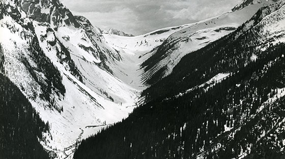 Black and white aerial view of valley surrounded by steep mountains in winter.