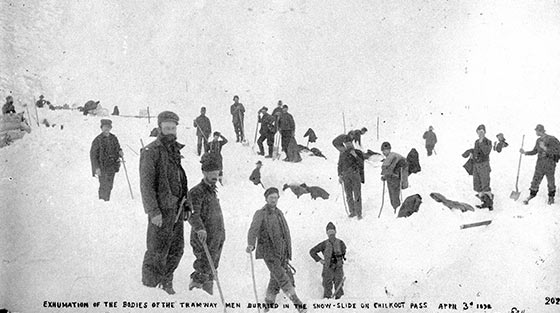 At least 20 men with shovels stand still for black and white photograph on the site of fatal snowslide.