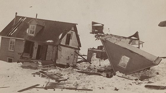 Photographie en noir et blanc montrant les restants d'une maison à deux étages dans la neige, coupée en deux avec le toit arraché.