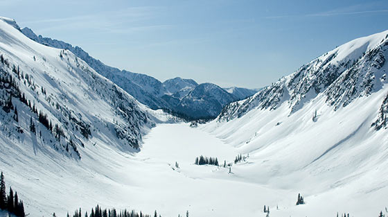 Aerial, colour photograph of snow covered valley surrounded by mountains.