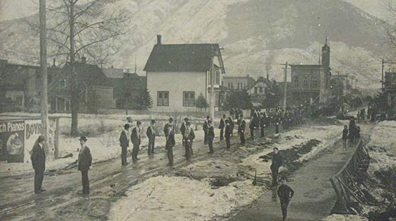 Black and white photograph of 100 + people lining up for funeral procession on street in snow.